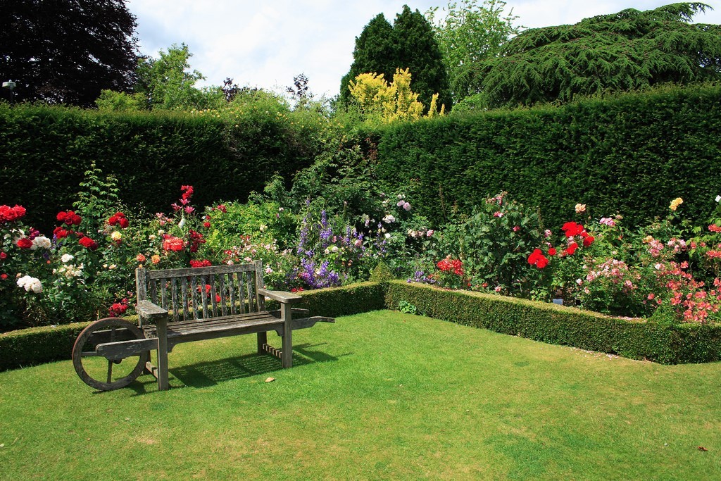 A beautiful, manicured garden featuring a stone pathway and a seating area, surrounded by lush greenery.